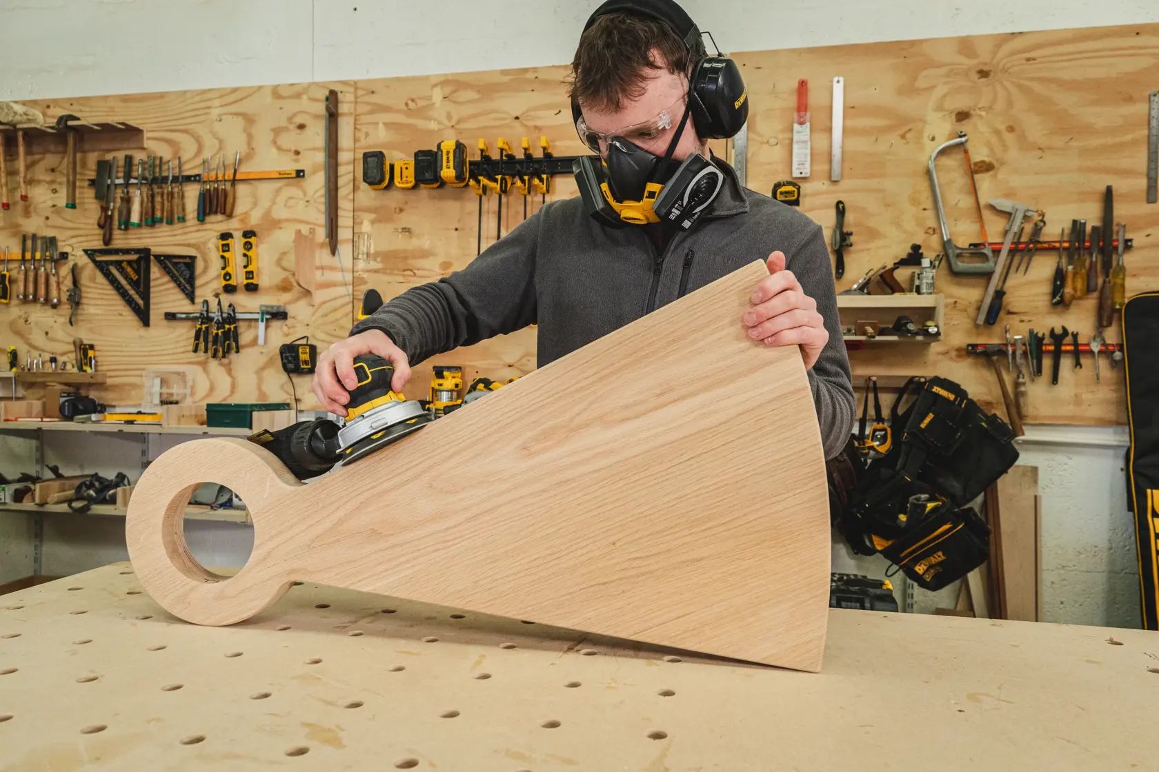 Person using a DEWALT sander on a large wooden piece in a workshop.