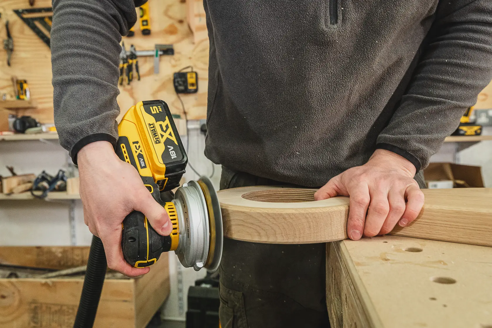 Person uses DEWALT cordless sander to smooth a wooden piece in a workshop.