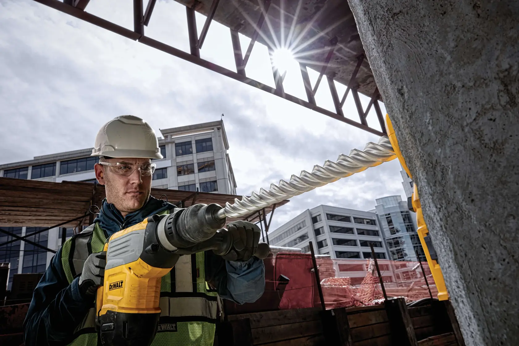 DEWALT rotary hammer drill in use on a construction site with concrete and steel beams in the background.