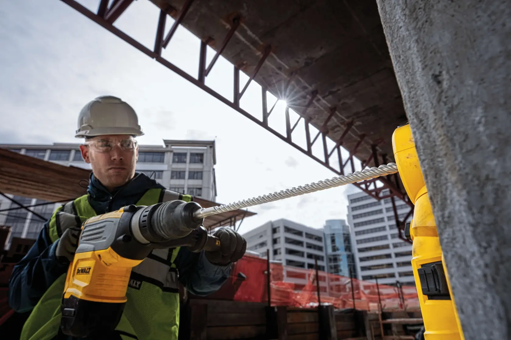 DEWALT rotary hammer drill in use on a construction site, drilling concrete with a spiral bit.