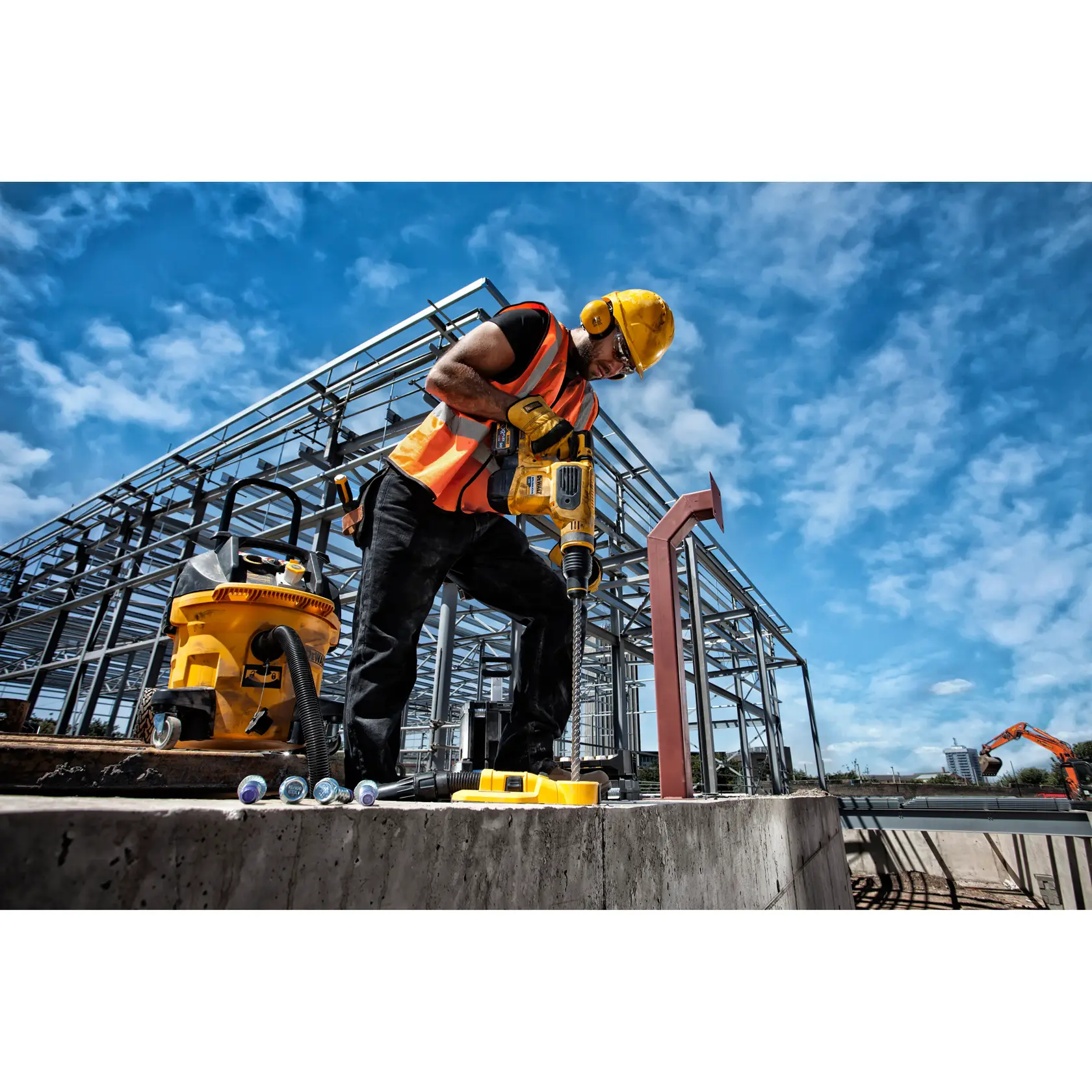 Worker uses DEWALT drill at construction site with steel frame and blue sky in the background.