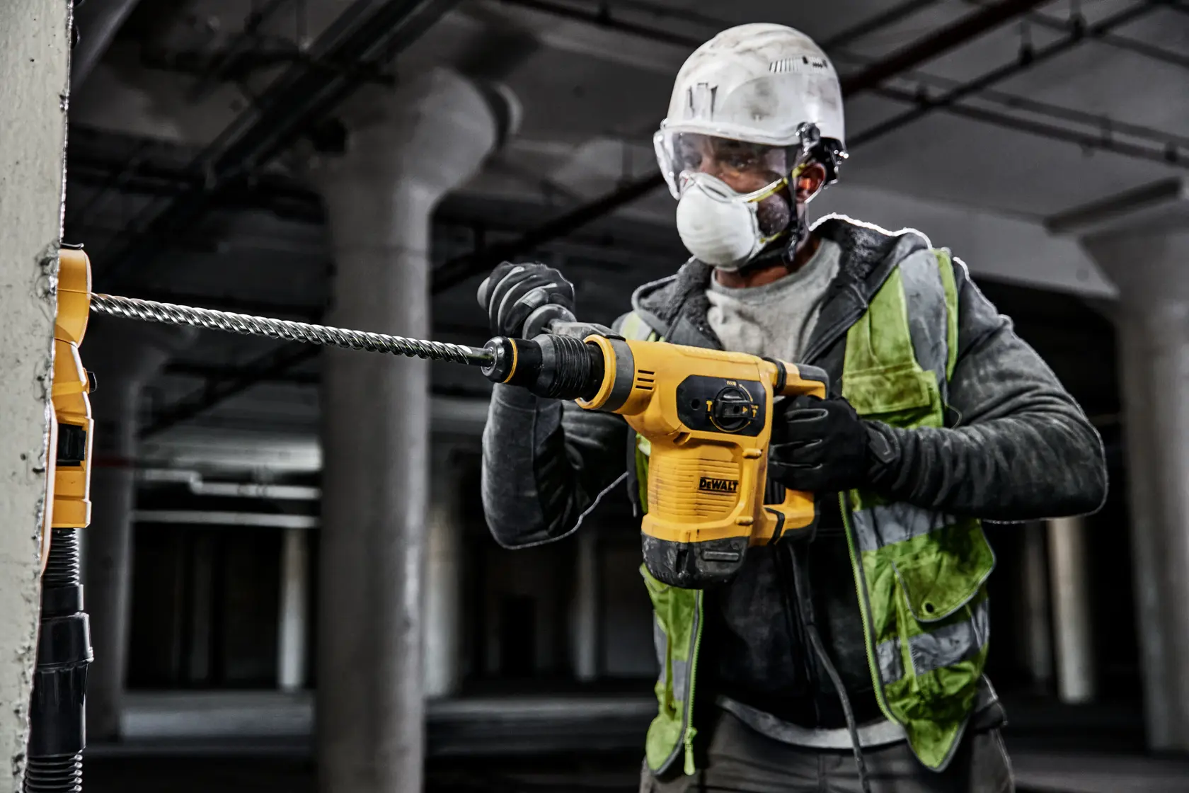 Person uses a DEWALT rotary hammer drill with DT60827 bit on concrete at a construction site.