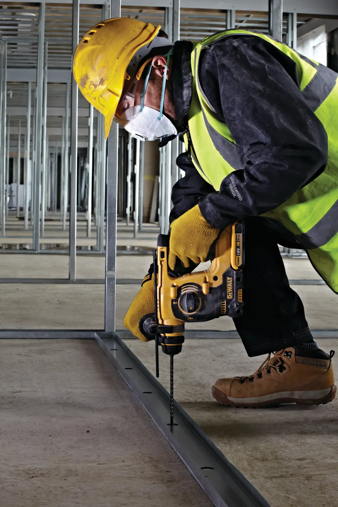 Worker uses DEWALT drill to drill metal frame on construction site, wearing safety gear and high-visibility vest.