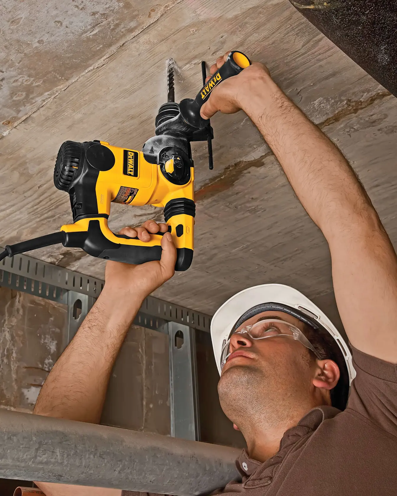 Person using a DEWALT drill to make a hole in a ceiling while wearing a hard hat and safety gear.