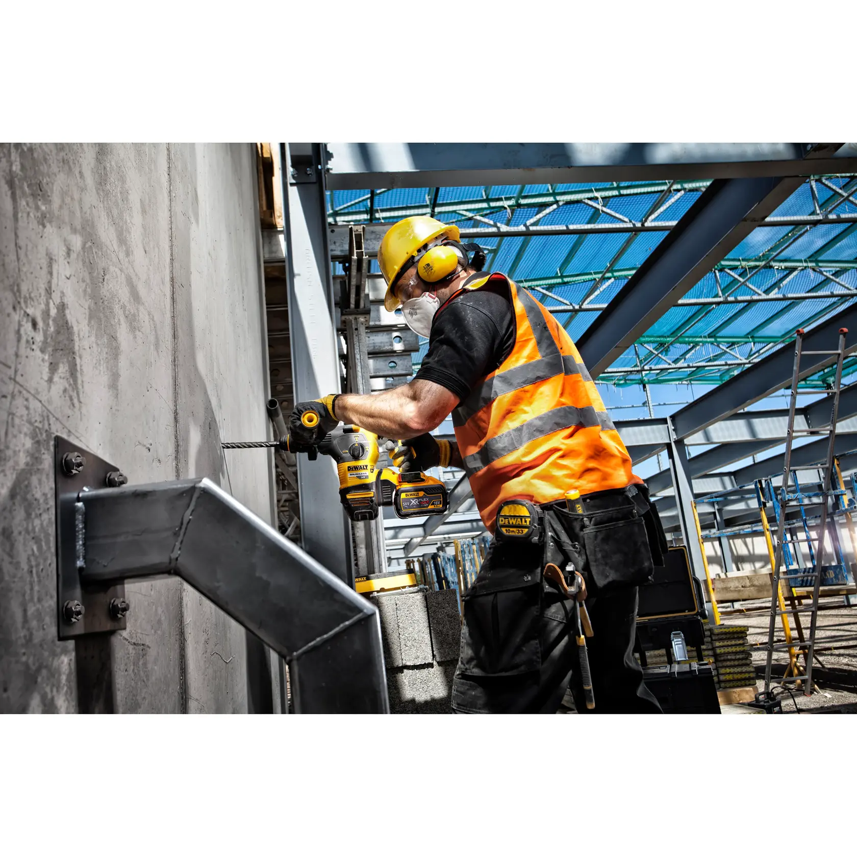 Worker in safety gear uses a DEWALT drill on a concrete wall at a construction site with metal beams.