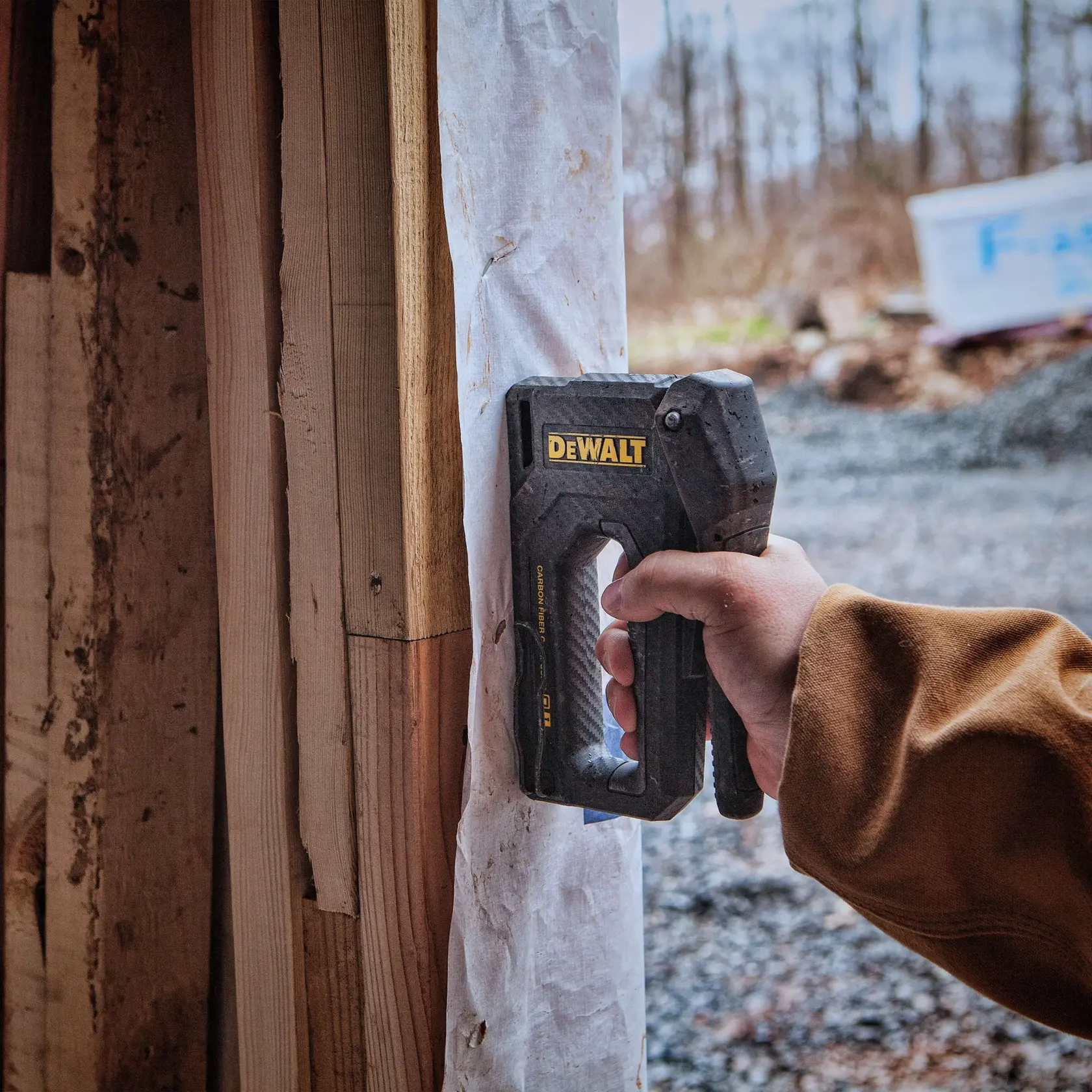 A person uses a DEWALT hand stapler to attach a sheet of material to a wooden frame at a construction site outdoors.
